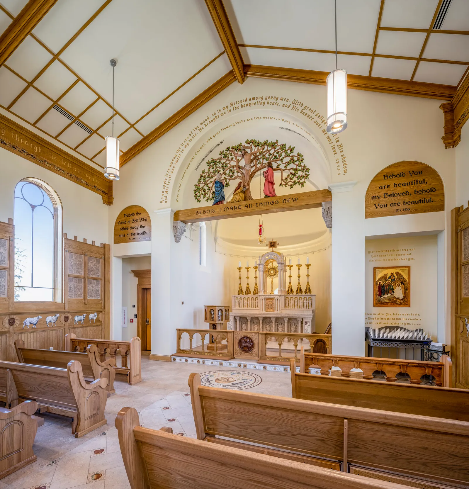 Wide-angle interior view of a wood-and-white chapel with pews, arched windows, and a marble altar beneath a tree-of-life relief.