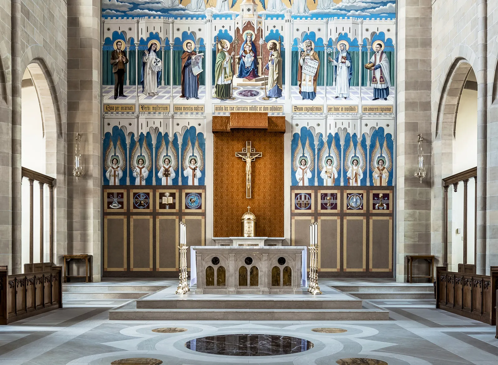 The restored sanctuary wall: the painted reredos of saints in blue and gold either side of the crucifix, the marble altar and tabernacle below.