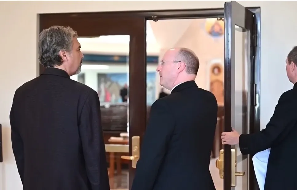 William Heyer in conversation with a priest at the open doors of a church, the sanctuary visible behind them