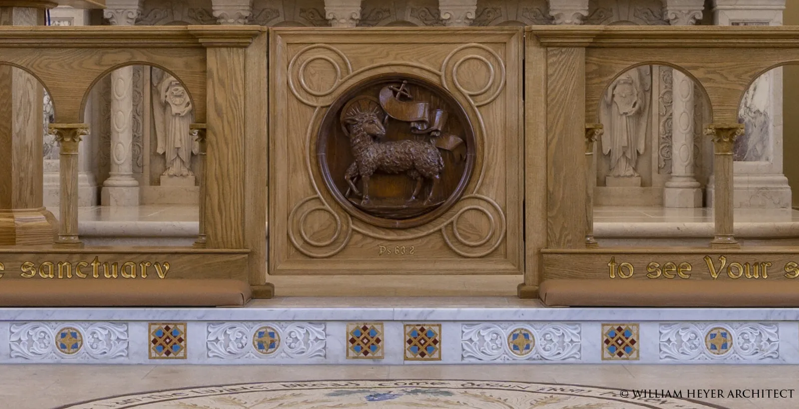 Detail of the carved oak altar rail: the Lamb of God in a roundel between arcaded panels, above a marble step inlaid with colored tiles.