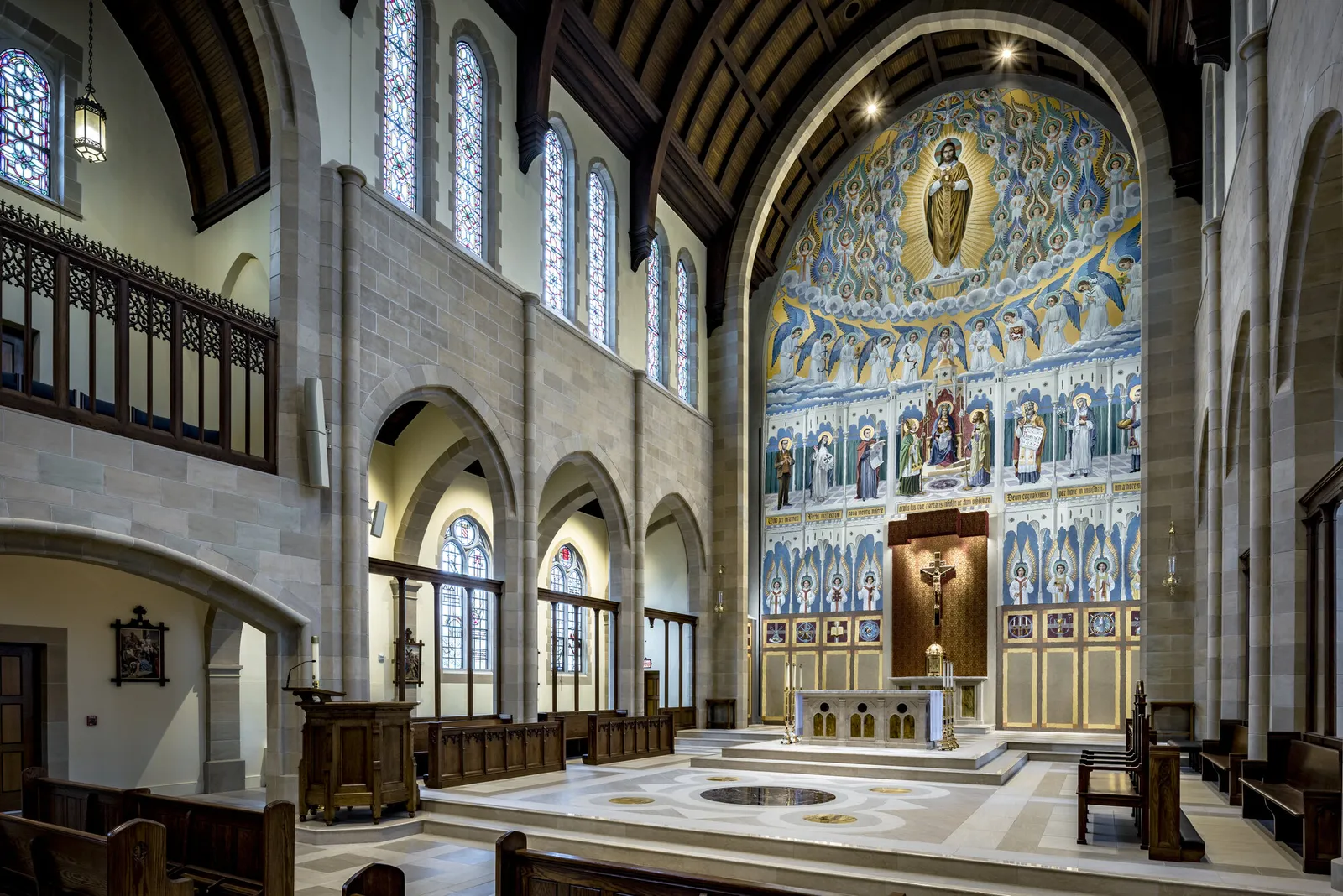 The sanctuary seen from the side aisle: the painted apse arch and reredos, the timber roof and the stone piers.